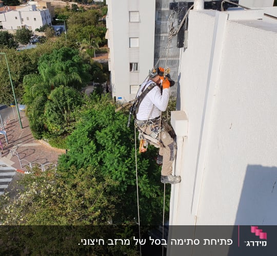אדם בעבודת גובה על קיר בניין עם ציוד בטיחות